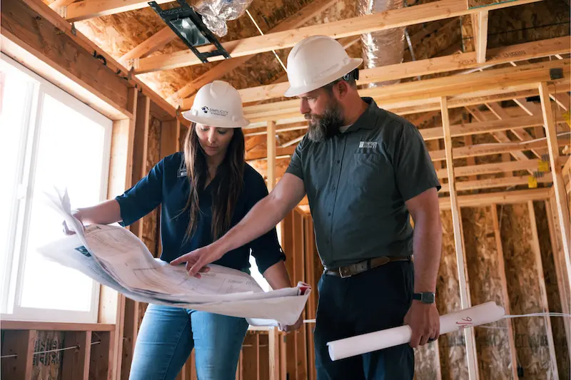Two contractors pointing at a blueprint inside of a under construction house