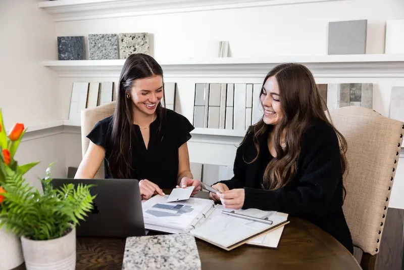 Two ladies sitting at a table inside of a design studio looking at swatches
