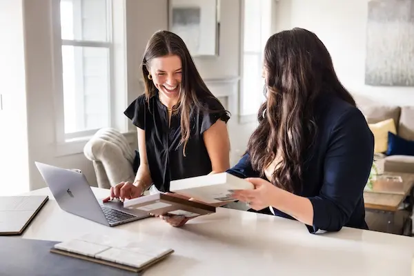 A woman in a beige sweater and long dark hair is smiling while reviewing a fan of paint swatches in her hand at a design studio.