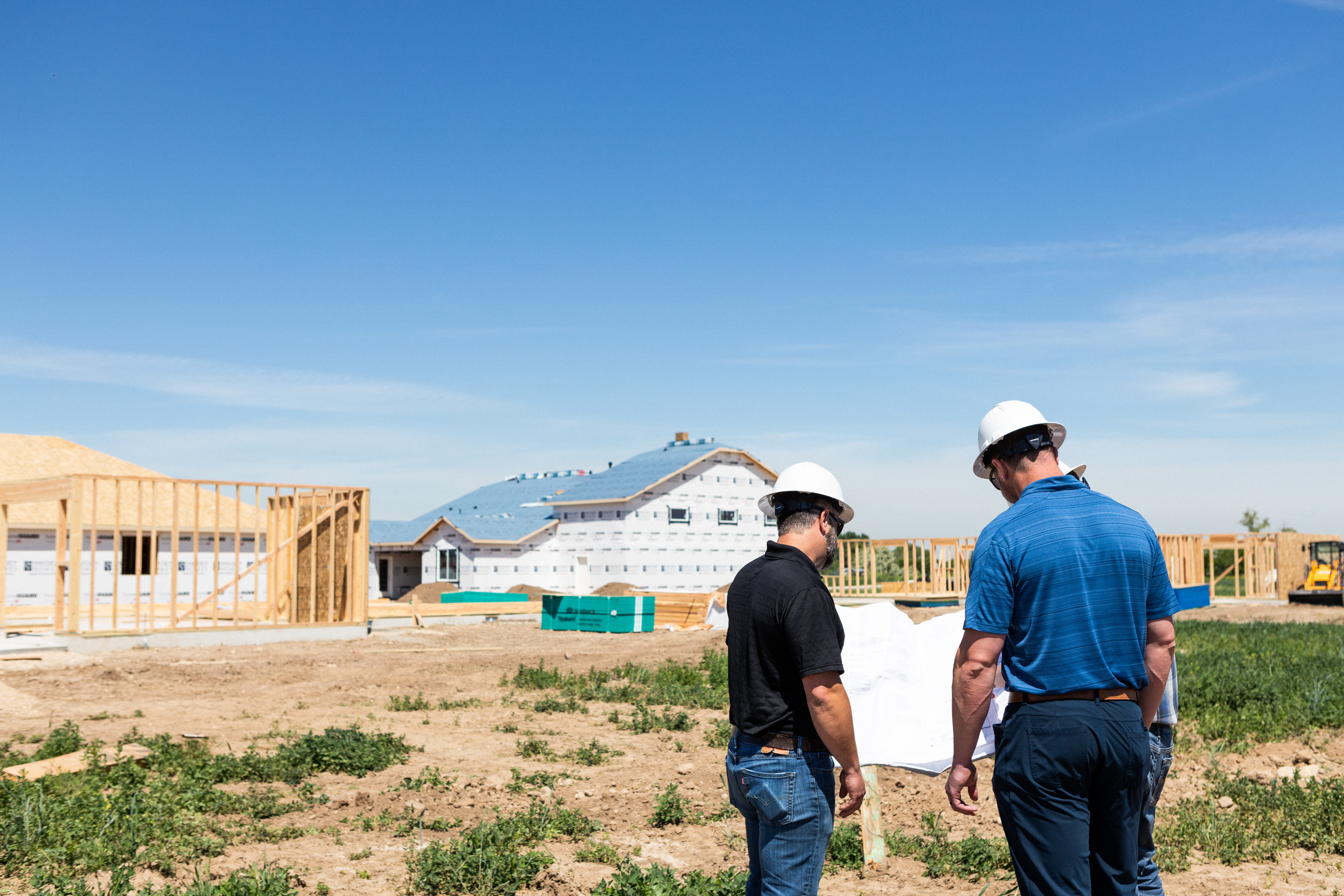How to Buy Land to Build a New Home. Two Simplicity Homes employees standing on a construction lot looking at building plans